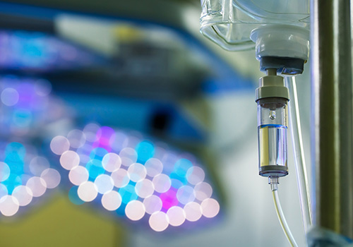 Functioning IV drip hanging on a pole in hospital with LED surgical lights in the background. Patient illness treatment hospital medicine and healthcare abstract and concept.
** Note: Shallow depth of field